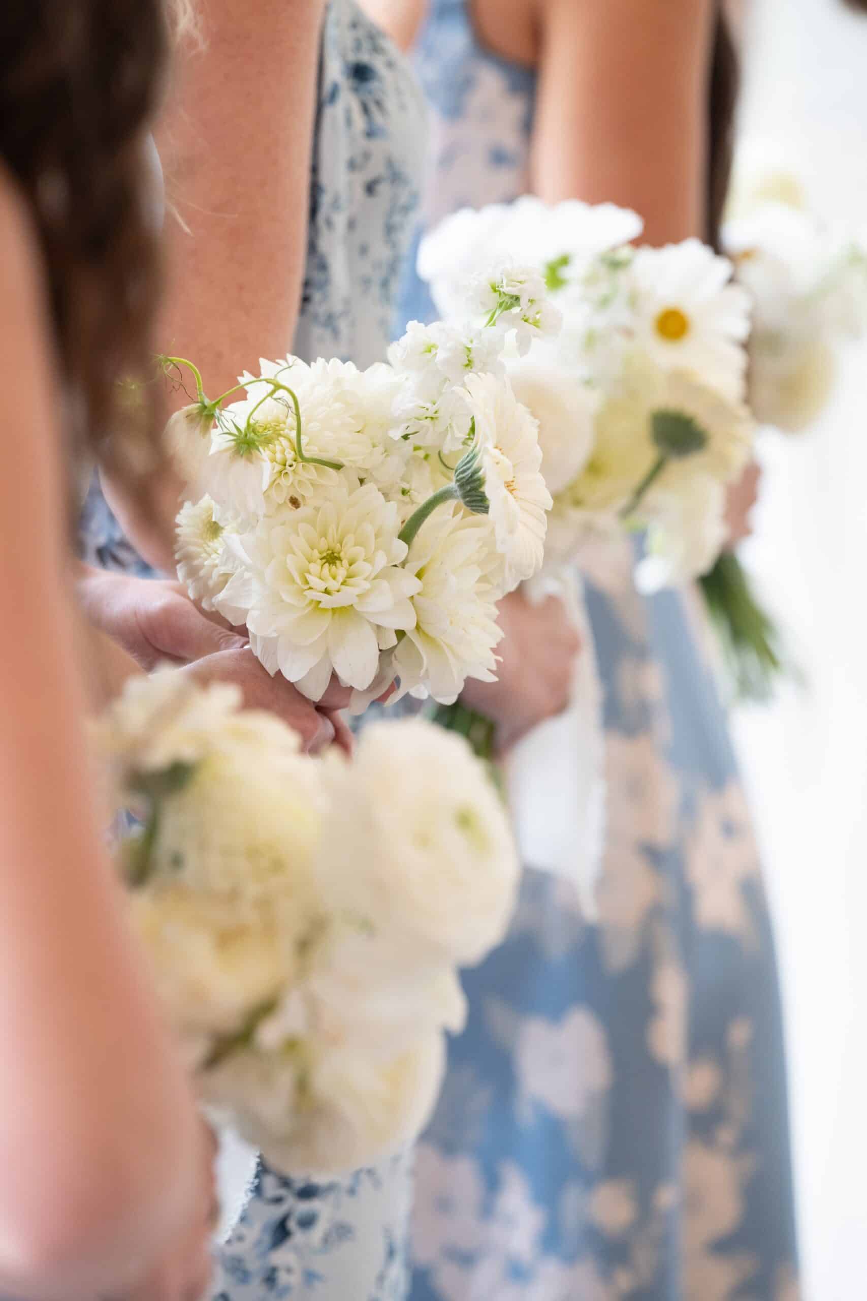 Des demoiselles d'honneur alignées portent des bouquets blancs de dahlias et de renoncules sur des robes bleues claires. Scène de mariage.