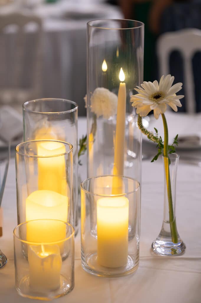 Centre de table de mariage : bougies LED chaleureuses dans des vases en verre, éclairant une élégante gerbera blanche. Ambiance intime.
