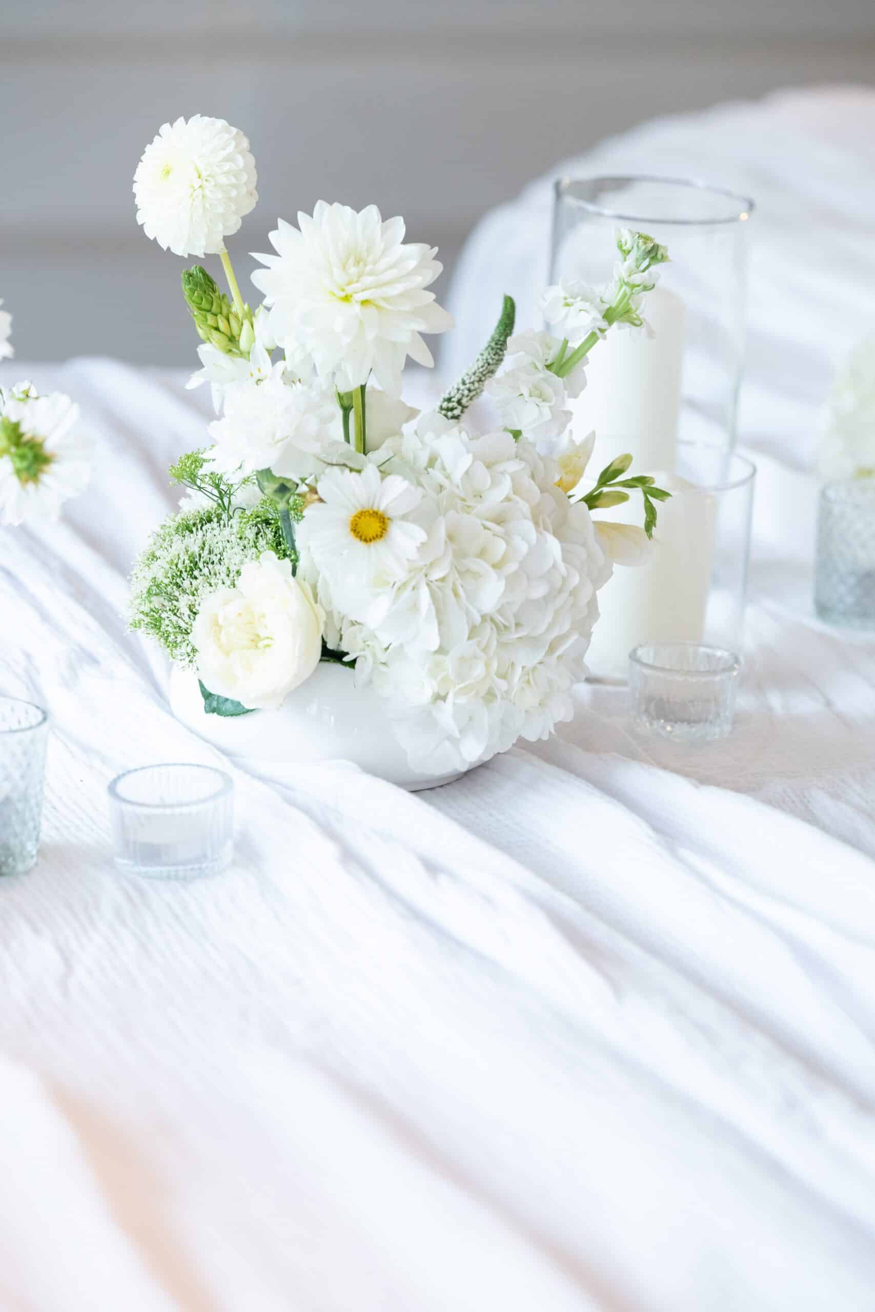 Arrangement floral blanc composé d'hydrangées et de dahlias, servant de centre de table élégant avec des bougies votives.