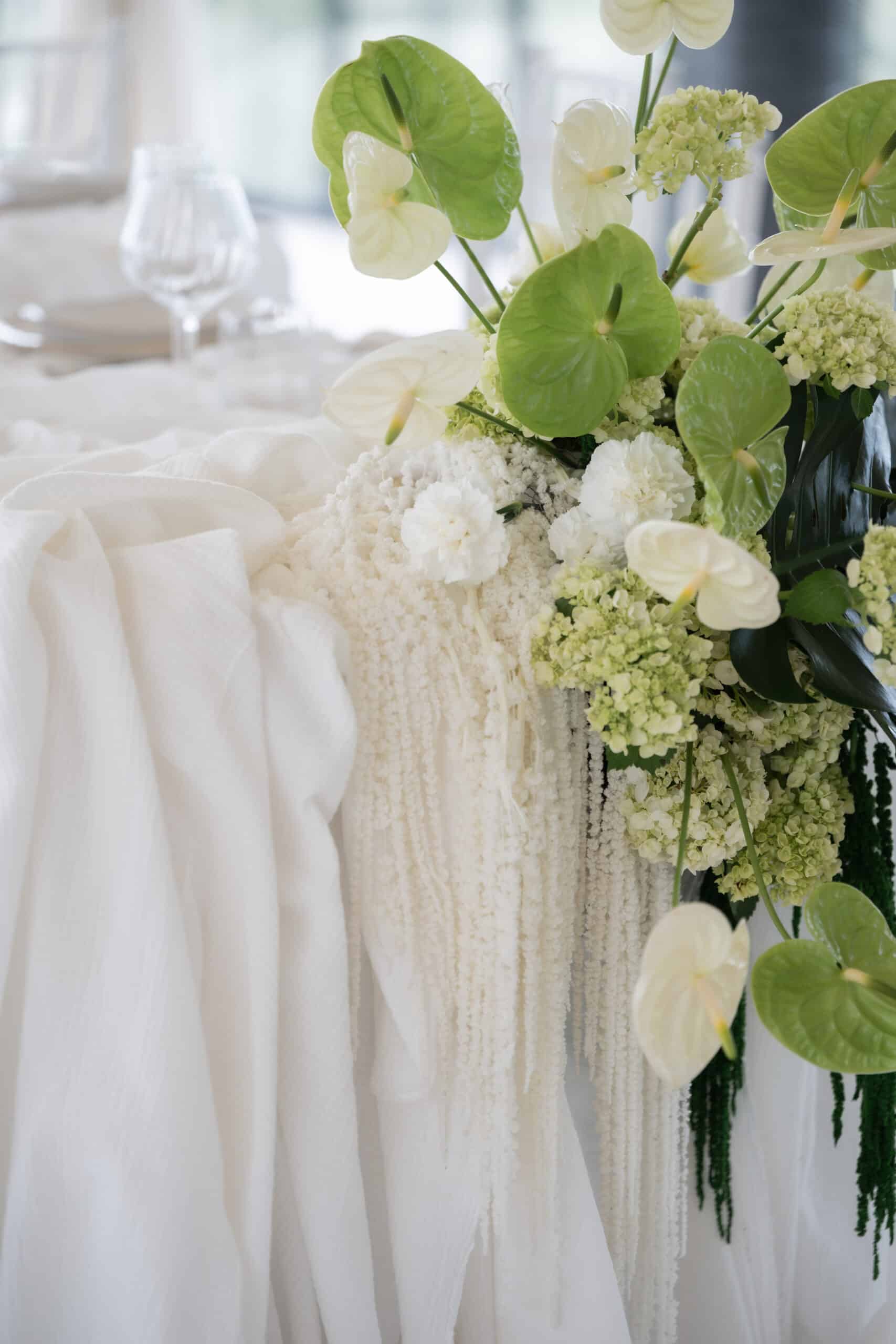 Centre de table élégant d'anthuriums verts et blancs, hortensias lime et amarante retombante, sur nappe blanche texturée.