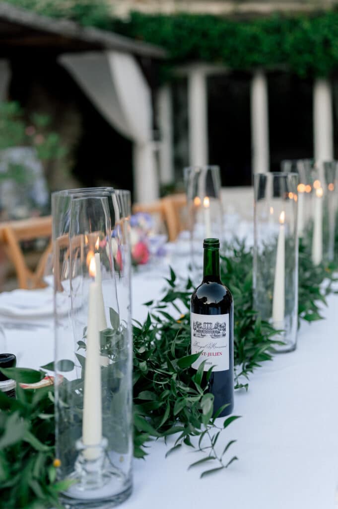 Longue table de réception avec guirlande de verdure, bougies allumées sous verre et vin Saint-Julien Royal Marceau 2018, créant une ambiance élégante.