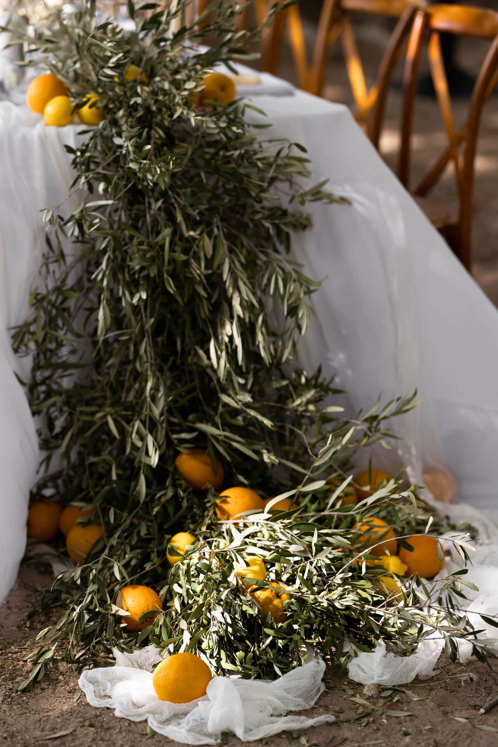 Cascade d'olivier et agrumes sur une table de mariage blanche. Décoration rustique méditerranéenne avec oranges et citrons au sol.