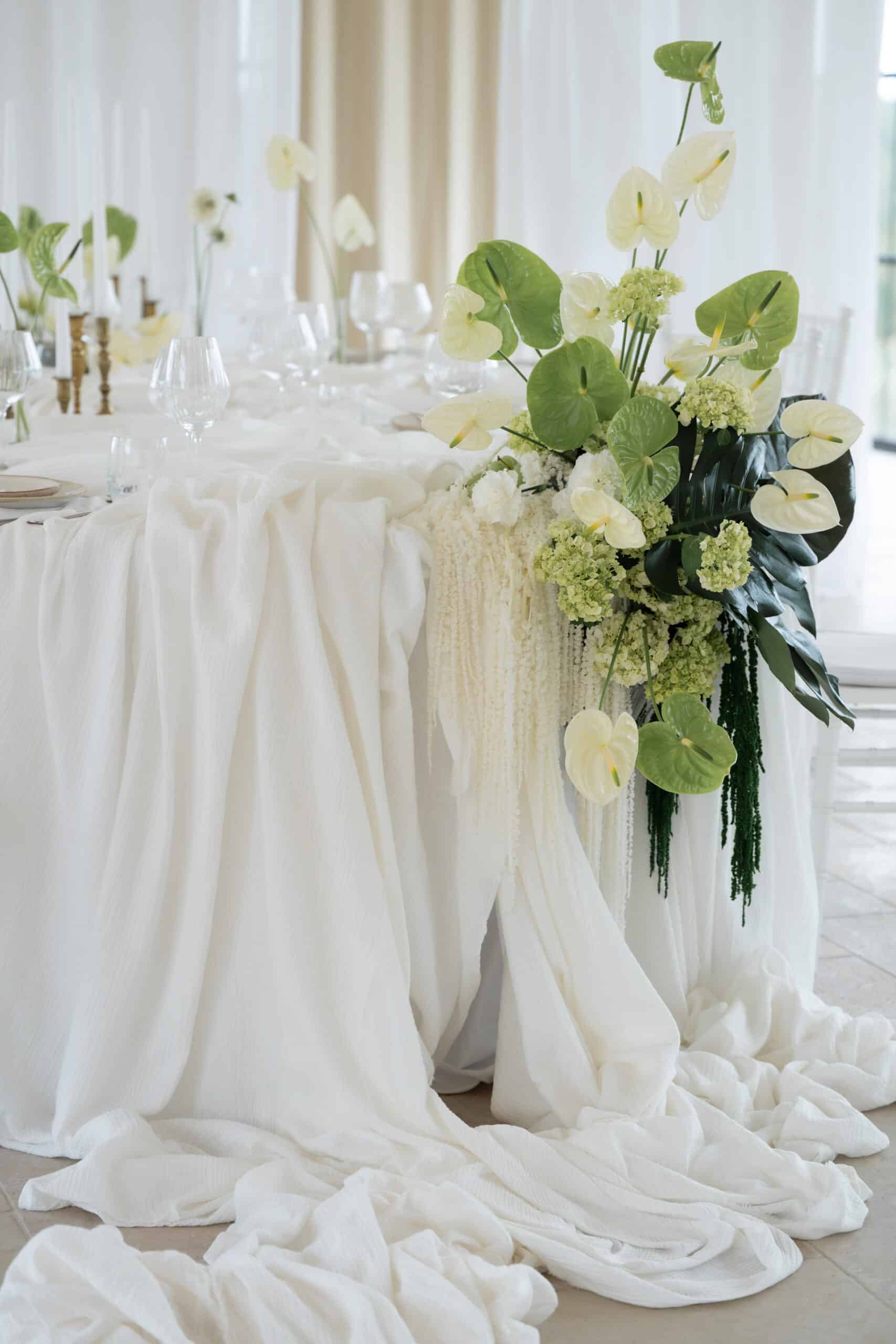 Table d'événement élégante : nappage blanc drapé, Anthuriums (verts et blancs) modernes, hortensias et chandeliers dorés.