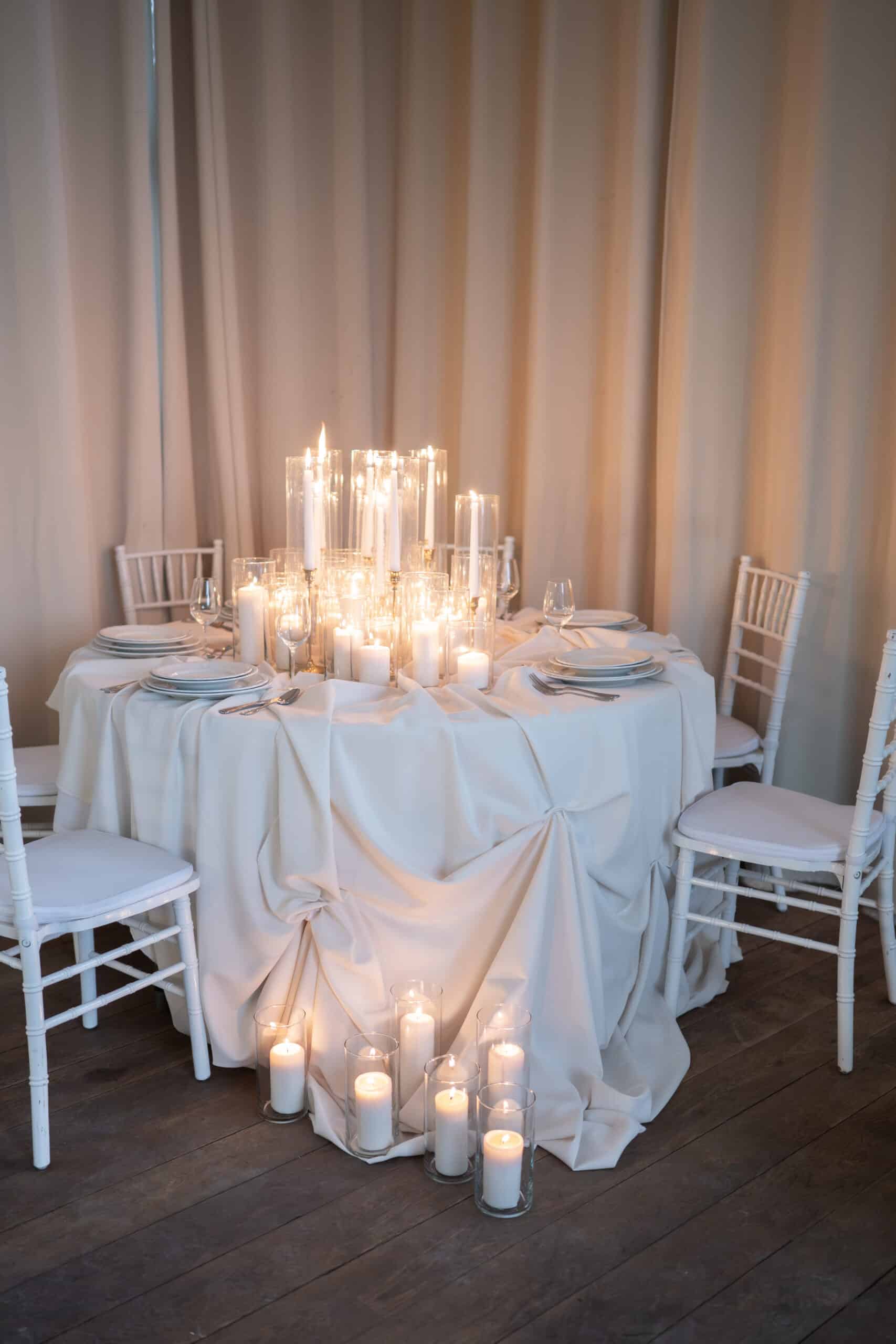 Magnifique table de réception avec un centre de table en bougies blanches et chandelles, créant une ambiance romantique. Chaises Chiavari blanches.