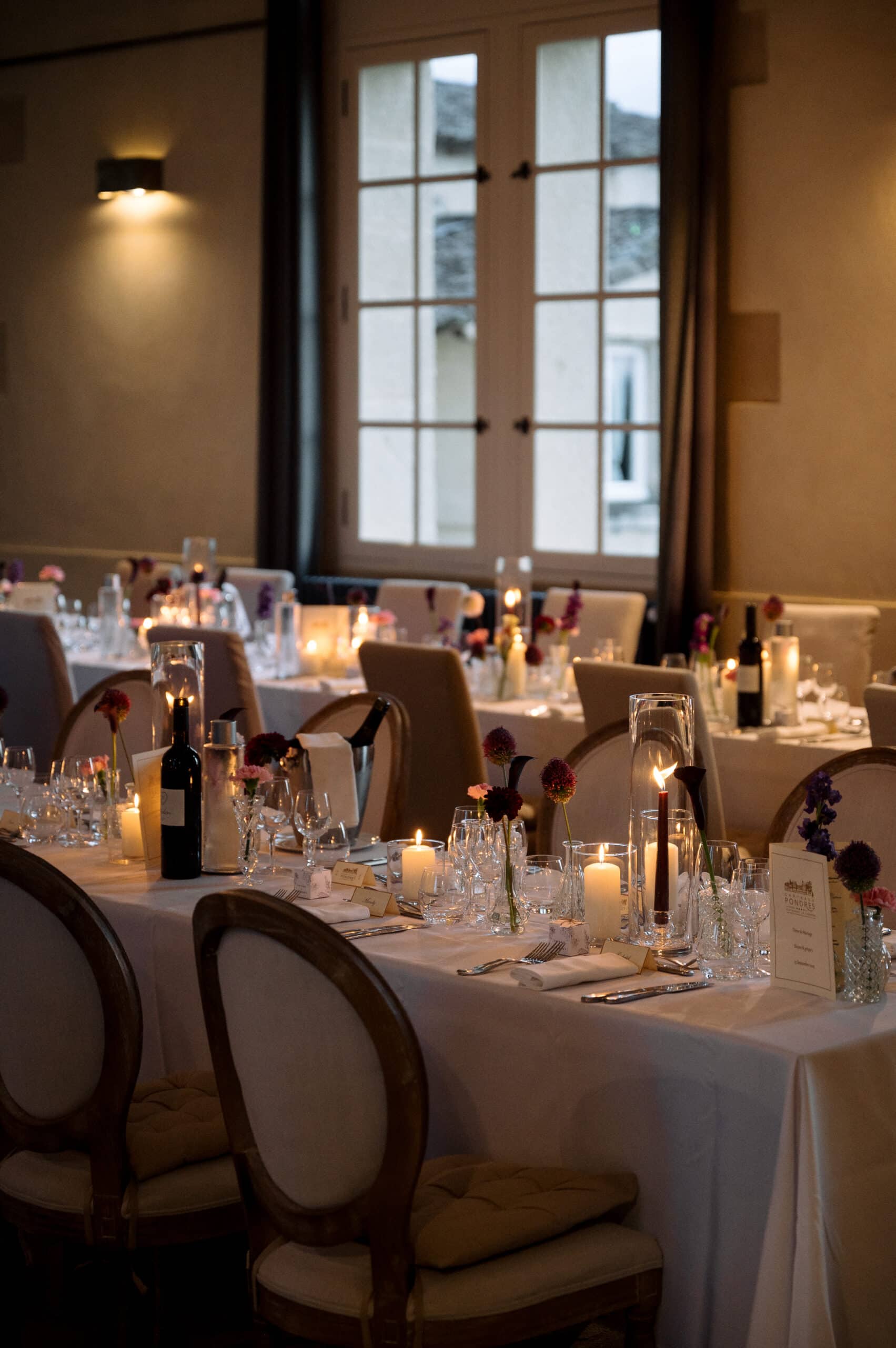 Dîner de Mariage au Château Pondres. Longues tables élégantes éclairées par des bougies, fleurs sombres et verres pour une ambiance intime.