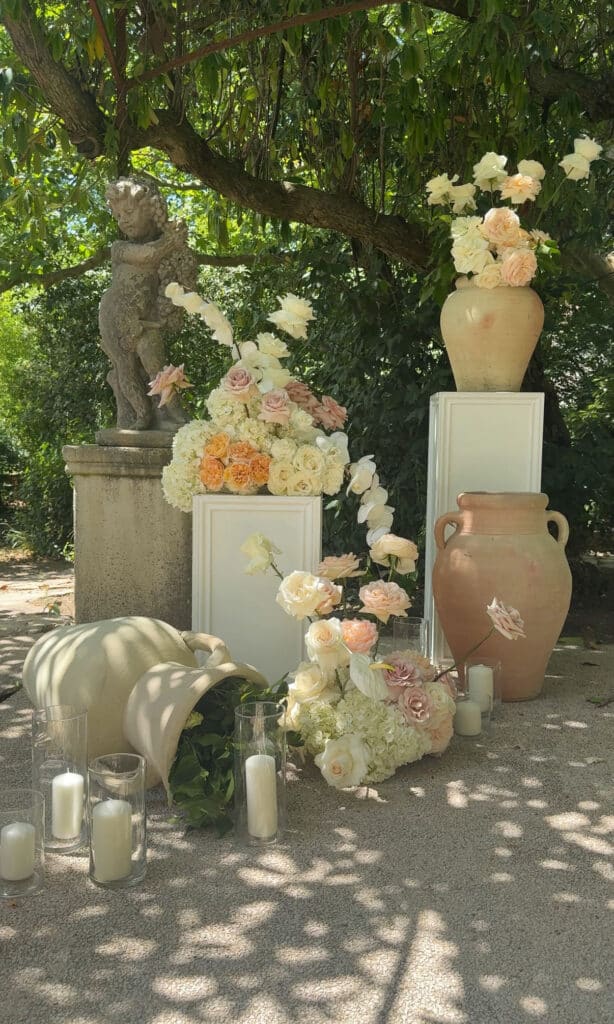 Arrangement de roses blanches et pêche, hortensias et vases en terre cuite. Décoration élégante de jardin avec statue de chérubin.